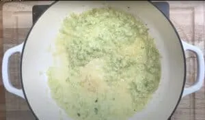 Chopped onions cooking in a white pot on a wooden board; preparation for a delicious homemade dish.